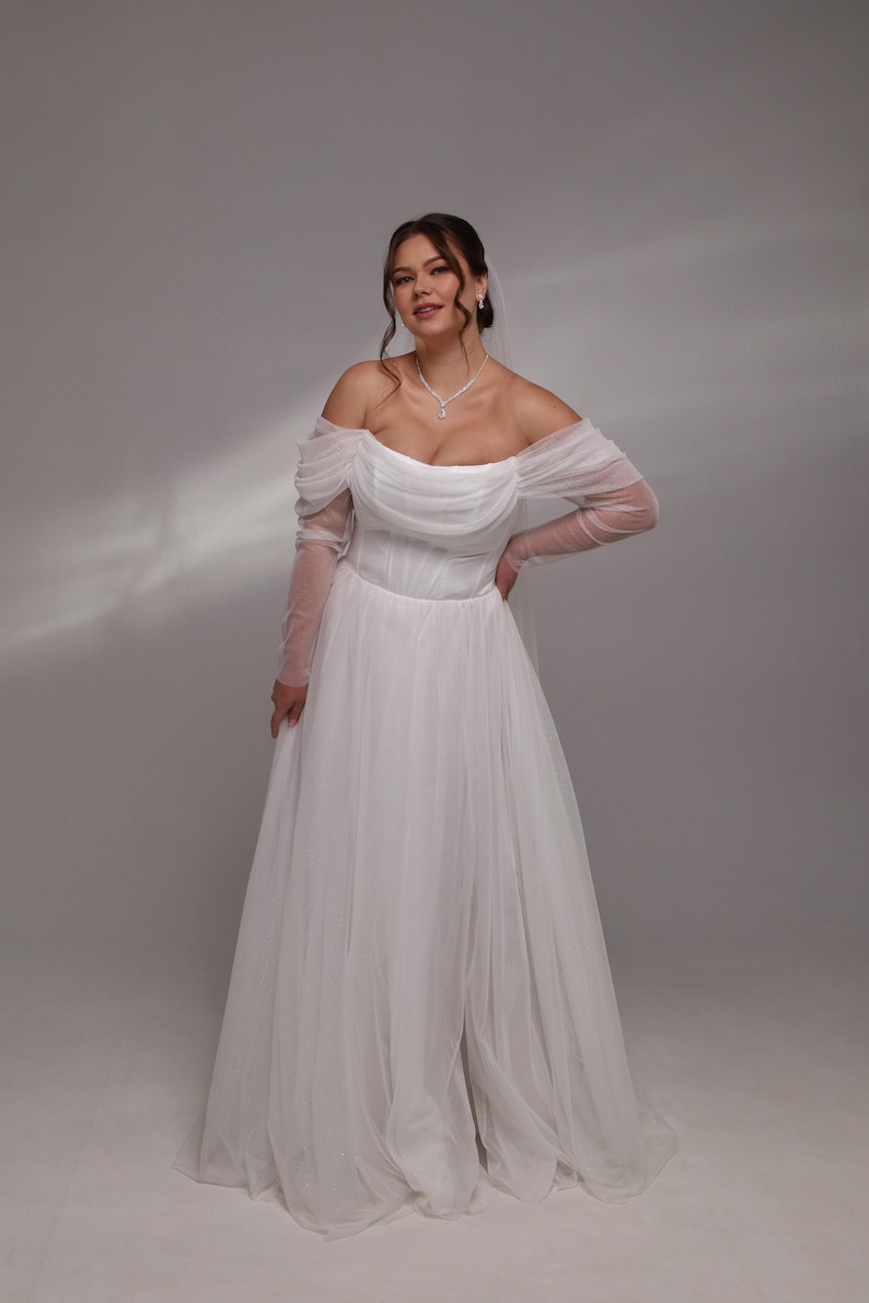 May include: A white off-the-shoulder wedding dress with long sleeves and a flowing skirt.
