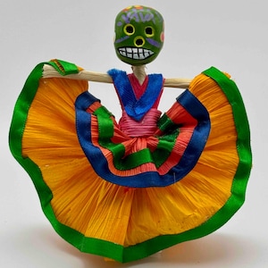 May include: A colourful Mexican folk art doll with a green skull head and a yellow, orange, green, blue and pink skirt.