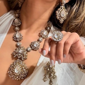 May include: An ornate jewelry set featuring a necklace, earrings, and a ring. The necklace has large, clear stones set in a detailed, antique-gold colored metal. The earrings and ring mirror the necklace's design, creating a cohesive and elegant look.