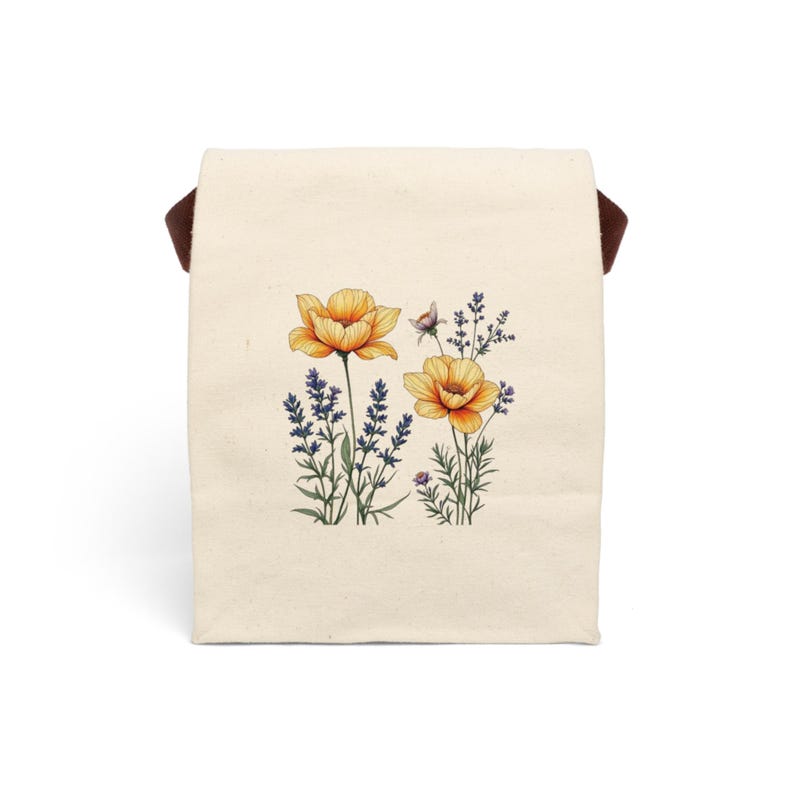May include: A white canvas tote bag with a brown handle. The bag has a floral design printed on the front. The design features two yellow flowers with purple stems and leaves. The flowers are surrounded by green leaves and stems.