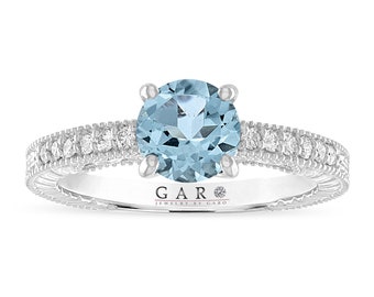 Könnte beinhalten: Ein silberner Verlobungsring mit einem runden Aquamarin als Mittelstück und einem Diamantenhalo. Die Ringschiene ist mit kleineren Diamanten besetzt.