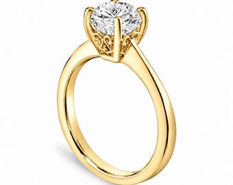 May include: A yellow gold ring featuring a round brilliant-cut clear gemstone set in a six-prong setting. The gallery of the setting displays intricate filigree metalwork, while the band is smooth, polished, and solid yellow gold.