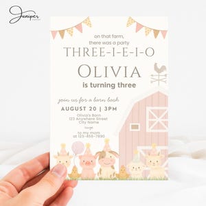 Pode incluir: Convite para uma festa com tema de fazenda. O convite apresenta o texto "THREE-I-E-I-O OLIVIA está fazendo três anos" e "junte-se a nós para uma festa no celeiro". O design inclui uma ilustração de celeiro rosa, animais de fazenda e uma faixa.