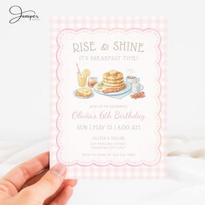Könnte beinhalten: Eine rosa-weiß karierte Einladung mit einem gewellten Rand. Die Einladung lautet "Rise & Shine, It's Breakfast Time!" und zeigt Illustrationen von Frühstücksspeisen. Sie kündigt Olivias 6. Geburtstag an, einschließlich Datum, Uhrzeit und Ort.