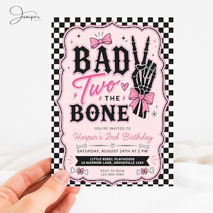 May include: A rectangular birthday invitation card featuring a black and white checkered border and a light pink center. The text reads BAD TWO THE BONE with a skeleton hand making a peace sign, pink bows, and event details for Harper's 2nd Birthday.