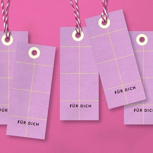 Könnte beinhalten: Mehrere lavendelfarbene Geschenkanhänger mit einem Rastermuster und den Worten "FÜR DICH" in Schwarz gedruckt. Jeder Anhänger wird von einer weiß-rosa Schnur gehalten, mit einem rosa Hintergrund.