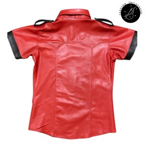 May include: A red leather short-sleeve shirt with black accents on the collar and sleeves. The shirt has a classic collar and shoulder epaulettes. The Fashion Influencer logo is in the upper right corner.