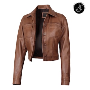 May include: A brown leather jacket with a collared neckline, two chest pockets, and button closures. The jacket has long sleeves and a cropped length. The interior lining is dark. The jacket is a classic style.