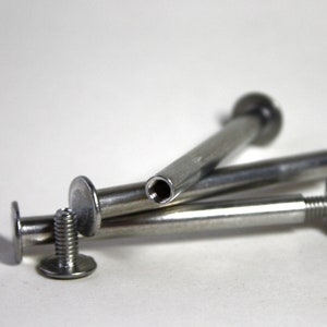 May include: Three silver metal screws with a flat head and a threaded shaft. The screws are arranged in a pile, with the heads facing up.