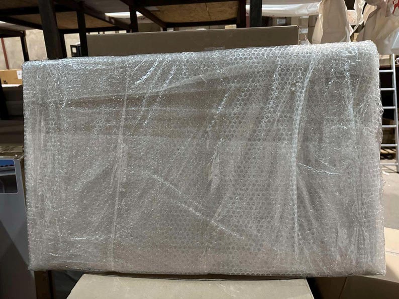 May include: A rectangular object wrapped in clear bubble wrap. The object is large and appears to be a piece of furniture or a similar item, ready for shipping. The bubble wrap provides protection during transit.
