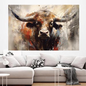 May include: A large canvas print of a bull's head, rendered in an abstract style. The artwork features a palette of browns, oranges, and grays, with the bull's horns prominently displayed. The painting is mounted on a white wall above a light-colored sofa.