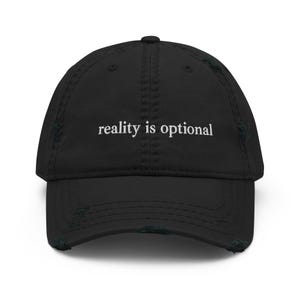 Könnte beinhalten: Schwarze Baseballkappe mit weißem Text "reality is optional". Die Kappe hat einen gebogenen Schirm und einen abgenutzten Look. Der Hut ist ein klassisches Sechs-Panel-Design.