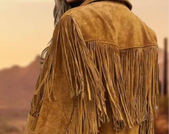 May include: A brown suede jacket with long fringe detailing on the back and sleeves. The jacket has a collar and a button closure. The image shows the back of the jacket, with a desert landscape in the background.