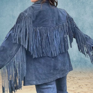Peut inclure: Une veste en daim bleu avec des d&eacute;tails en franges sur les &eacute;paules, le dos et les manches. La veste a un col classique et une fermeture &eacute;clair sur le devant.