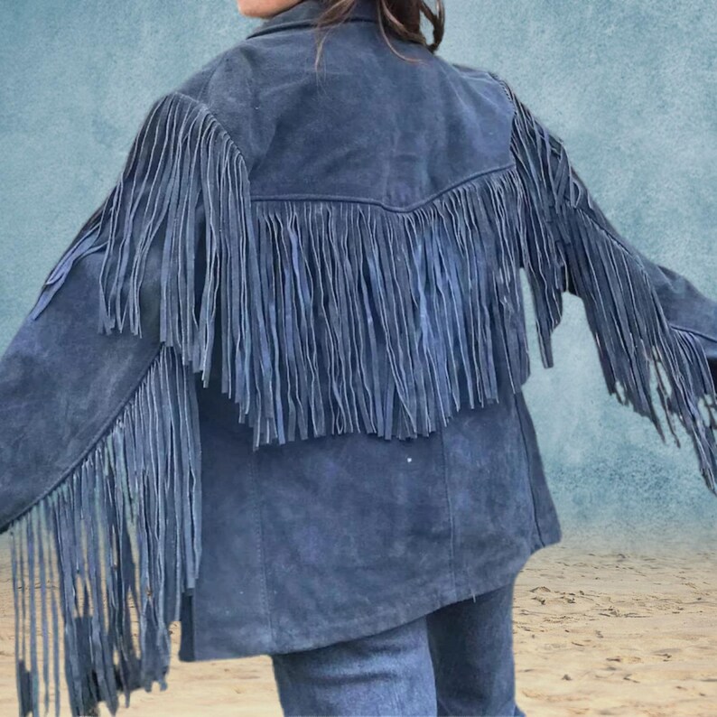 Peut inclure: Une veste en daim bleu avec des d&eacute;tails en franges sur les &eacute;paules, le dos et les manches. La veste a un col classique et une fermeture &eacute;clair sur le devant.