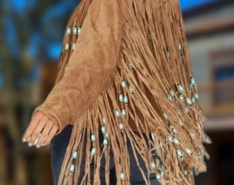 Op de afbeelding: Een bruin suède jack met franjes en turquoise kralen. Het jack heeft een lange, vloeiende stijl en is perfect voor een bohemian look.