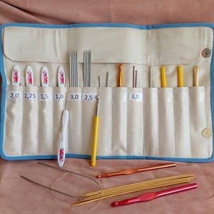 Könnte beinhalten: Eine blaue und weiße Stoffrolle mit verschiedenen Stricknadeln und Häkelnadeln. Die Rolle ist mit den Größen der Nadeln und Haken beschriftet, darunter 2.0, 1.75, 1.5, 1.0, 3.0, 2.5 und 3.0.