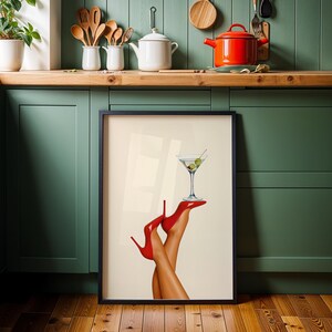 Print resting on the floor of a green kitchen with a wooden floor and red teapot nearby. The vibrant red shoes and martini contrast with earthy surroundings.