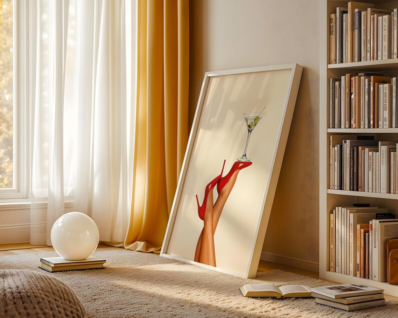 Artwork leaning against a bookcase in a cozy, golden-lit room. The red heels and martini glass catch sunlight on a textured beige blanket, adding glamour to the relaxed space.