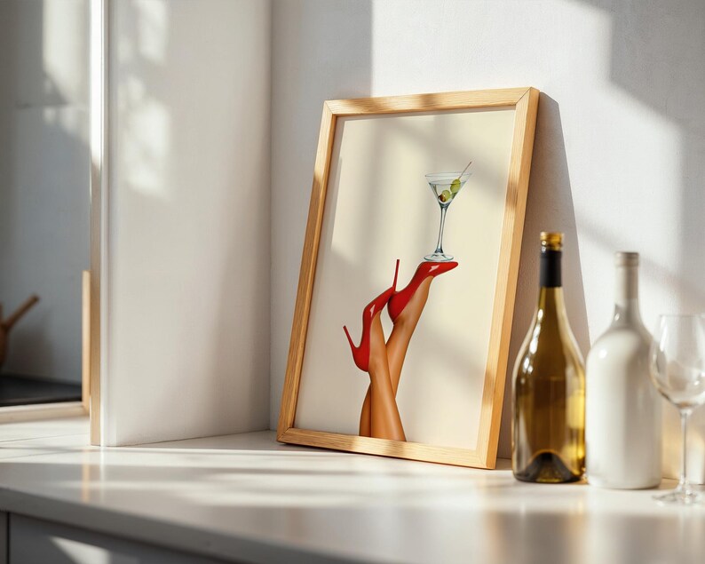 Framed print on a sunlit white table beside a wine bottle and glass. The red heels and martini glass are bright and elegant in a minimal dining setup.