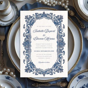 Könnte beinhalten: Eine Hochzeitseinladung mit blauem floralem Design und den Namen Isabelle Dupont und Etienne Moreau. Die Einladung liegt auf einem Tisch mit goldgeränderten Tellern, Besteck und Perlen. Der Text lautet "Samstag, 14. September 2025."