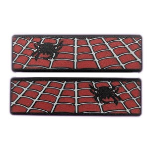 May include: Two rectangular patches featuring a red spiderweb design with a black spider in the center. The patches have a black border and are set against a white background.