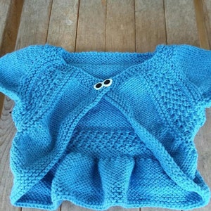 May include: A blue knitted cardigan with a ruffled hem and two white buttons.