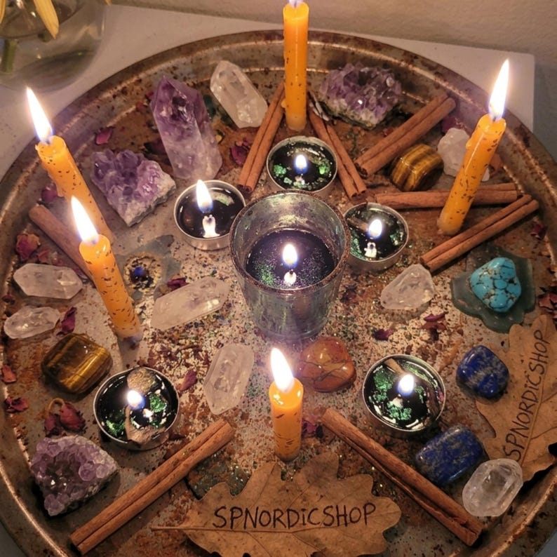 May include: A circular arrangement of candles, crystals, and cinnamon sticks on a rustic metal tray. Lit candles of varying sizes and colors, including tall yellow ones, surround a central glass with a lit candle. Amethyst and clear quartz crystals are also present.