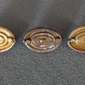 May include: Three oval-shaped brass cabinet knobs with a concentric circle design. The knobs have a slightly aged, antique look.