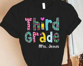 May include: Black t-shirt with the words "Third Grade" in colorful, patterned letters. A pink heart and pencil graphic are above the word "grade". The name "Mrs. Jones" is printed below the words.