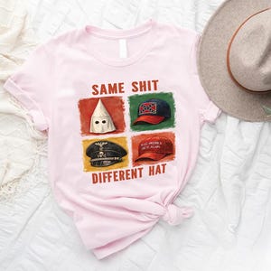 May include: Light pink t-shirt with the text "SAME SHIT DIFFERENT HAT" and four images of hats. A tan hat and greenery are in the background.
