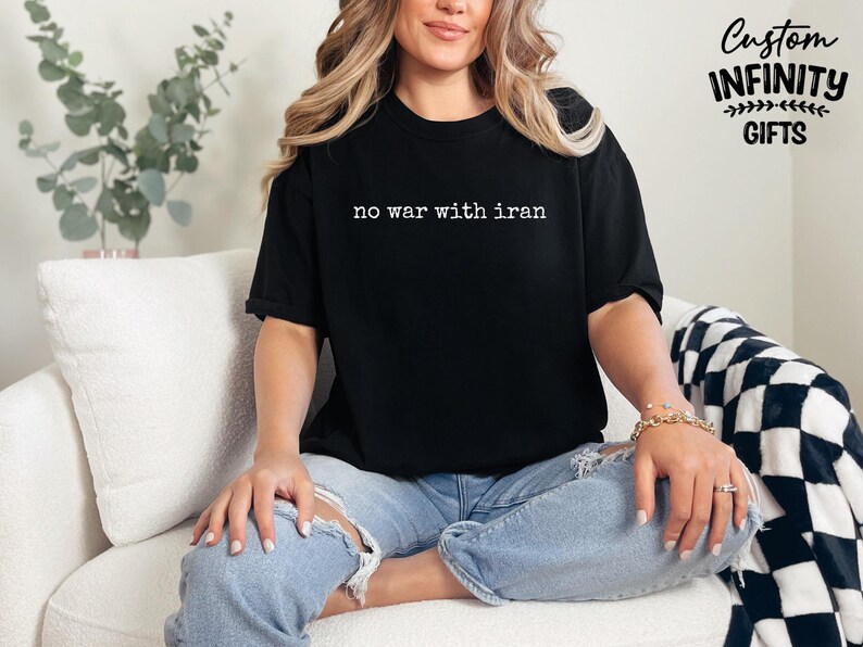 May include: Black t-shirt with the text "no war with iran" in white. The shirt is worn by a person sitting on a white couch. The words "Custom Infinity Gifts" are printed on the upper right corner.
