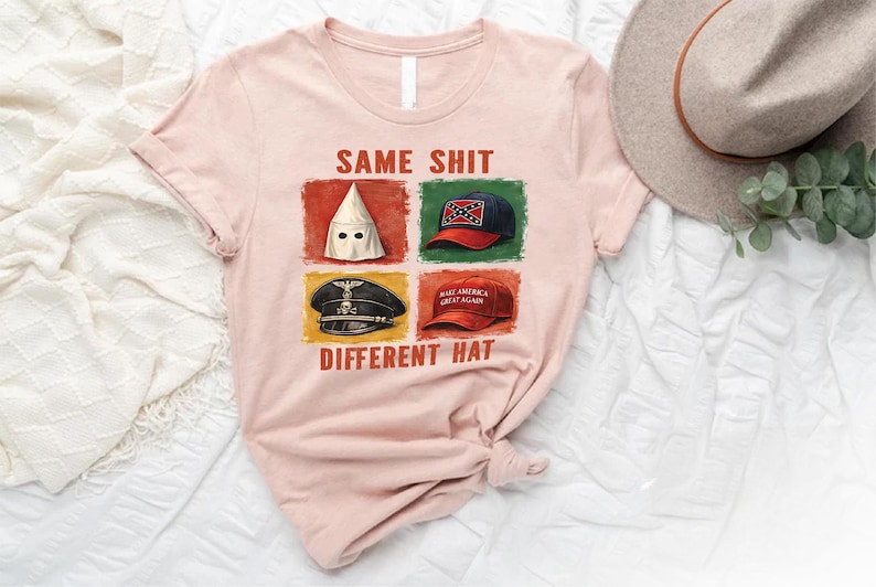 May include: A light pink t-shirt with the text "SAME SHIT DIFFERENT HAT" and images of a white hood, a Confederate flag hat, a Nazi hat, and a "Make America Great Again" hat.