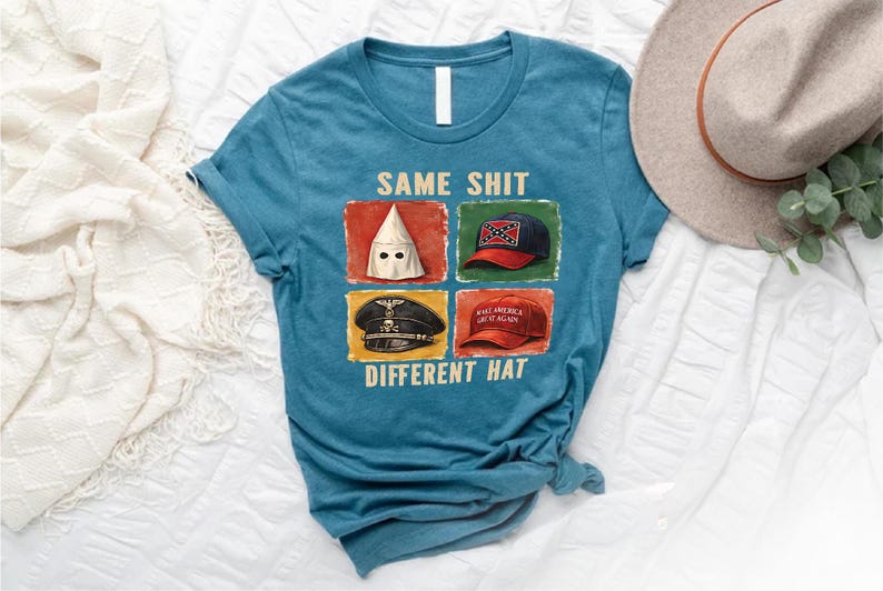 May include: Teal crew neck t-shirt with the text "SAME SHIT DIFFERENT HAT" and images of a KKK hood, a Confederate flag hat, a Nazi hat, and a "Make America Great Again" hat. A tan hat and greenery are in the background.