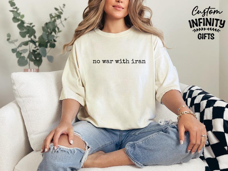 May include: Cream-colored t-shirt with the text "no war with iran" in a simple black font. The shirt is worn with blue jeans. The image also includes the text "Custom Infinity Gifts".