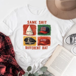 May include: White t-shirt with the text "SAME SHIT DIFFERENT HAT" and four images of hats: a white hood, a Confederate flag baseball cap, a Nazi cap, and a "Make America Great Again" hat. A red and black plaid shirt is visible.