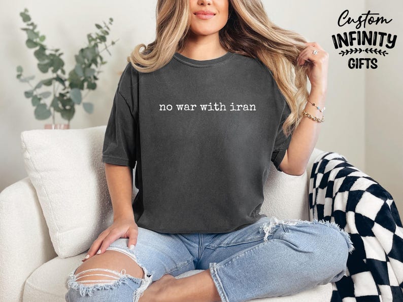 May include: Dark gray t-shirt with the text "no war with iran" in white. The shirt is worn with light blue ripped jeans. The image also includes the text "Custom Infinity Gifts".