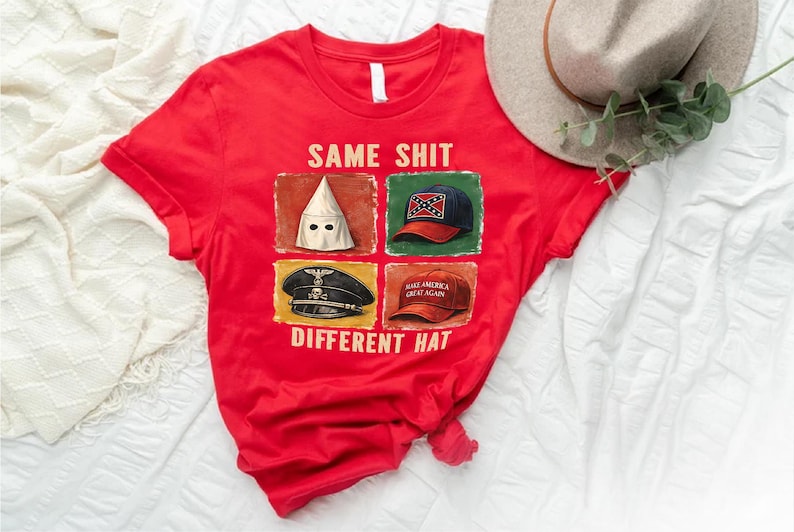May include: Red t-shirt with the text "SAME SHIT DIFFERENT HAT" and images of a KKK hood, a Confederate flag hat, a Nazi hat, and a "Make America Great Again" hat. A beige hat and greenery are in the background.