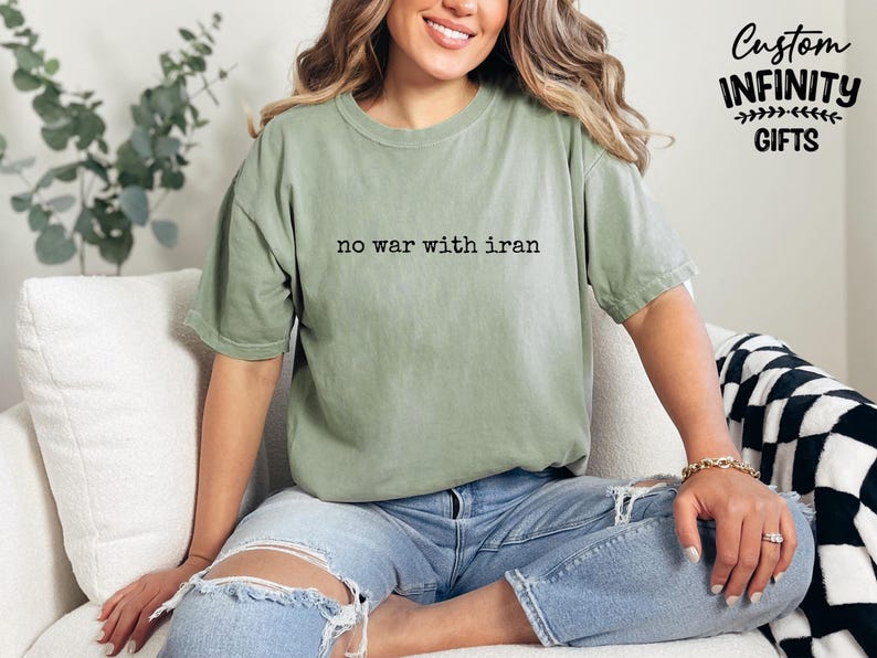 May include: A sage green t-shirt with the text "no war with iran" in black. The shirt is worn with blue jeans. The image also includes the text "Custom Infinity Gifts".