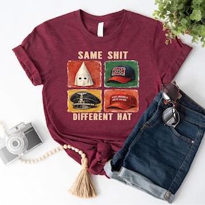 May include: Maroon t-shirt with the text "SAME SHIT DIFFERENT HAT" and four images of different hats. The shirt is paired with blue denim shorts and sunglasses. A camera and decorative beads are also in the image.