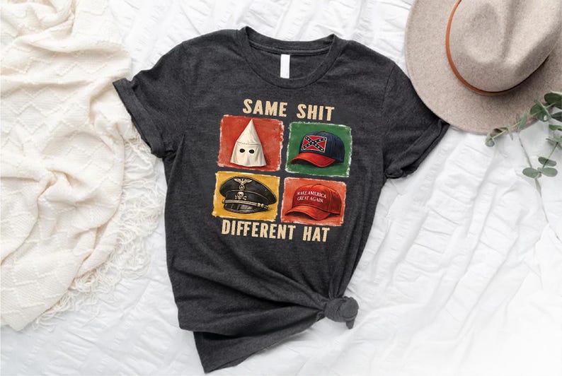 May include: Dark gray t-shirt with the text "SAME SHIT DIFFERENT HAT" and images of a KKK hood, a Confederate flag hat, a Nazi hat, and a "Make America Great Again" hat. A tan hat is in the background.