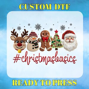 May include: A DTF transfer design featuring Christmas characters: a reindeer, snowman, gingerbread man, Christmas tree, and Santa Claus. The text reads "CUSTOM DTF", "#christmasbasics", and "READY TO PRESS". The design has a blue background.