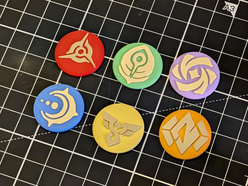 May include: A collection of seven colorful, circular tokens with various beige-colored symbols. The tokens are red, green, purple, blue, yellow, and orange. The tokens are arranged on a black grid.