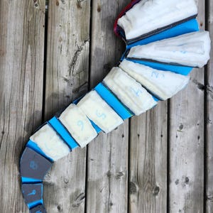 May include: A curved, segmented object in blue and white. It features white rectangular pads with blue numbers. The base is dark grey. The object rests on a wooden surface. The numbers are from 5 to 12.