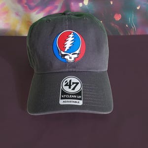 May include: A black baseball cap with a Grateful Dead Steal Your Face logo on the front. The cap has a 47 Clean Up adjustable strap on the back.