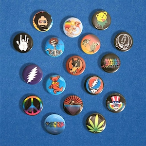 May include: A collection of colorful round buttons with various designs. The buttons feature images of a handprint, a skeleton, a bear, a peace sign, a wolf, a skull, a rainbow, and a cannabis leaf. The buttons are on a blue surface.