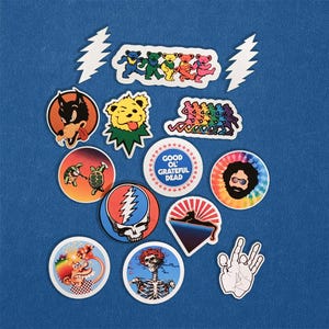 May include: A collection of colorful stickers featuring various designs. Included are dancing bears, a wolf, a bear with a green tongue, a turtle, a skull with a lightning bolt, a tie-dye face, and a hand making a peace sign.