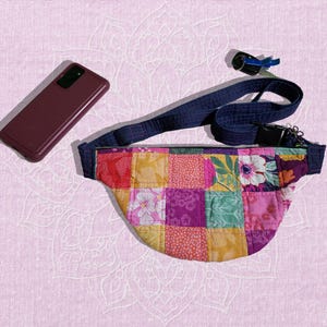 May include: A patchwork fabric fanny pack with a blue adjustable strap. The fanny pack has a variety of colors and patterns, including pink, yellow, green, and red.