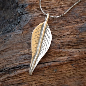 May include: A silver necklace with a leaf-shaped pendant. The pendant is textured and has a gold finish.