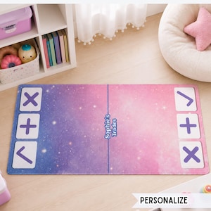 May include: A rectangular play mat featuring a pink and purple galaxy-themed background with white star patterns. The mat has a central blue line with the text "Sophie's Trades" and three white square icons on each side displaying purple symbols.